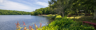 Sunshine glimmers across a lake framed by the lush greenery of Yale's Outdoor Education Center
